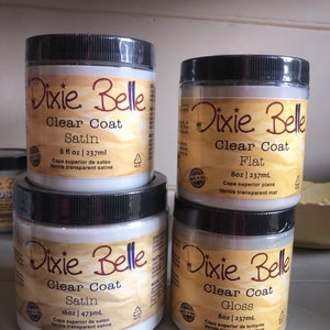 May include: Four bottles of Dixie Belle Clear Coat paint in satin, flat, and gloss finishes. The bottles are labelled with the Dixie Belle logo and the size and finish of the paint. The bottles are arranged in a pyramid shape.