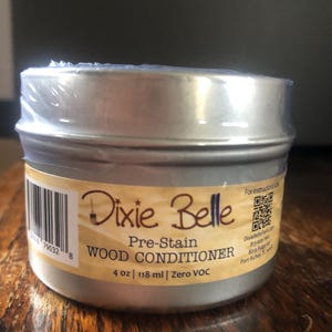 May include: A silver tin container with a white label that reads "Dixie Belle Pre-Stain WOOD CONDITIONER 4 oz | 118 ml | Zero VOC".