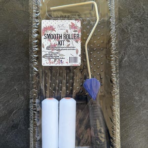 May include: A smooth roller kit in plastic packaging containing a black mini roller tray, a metal handle with a blue and black grip, and two white foam rollers. The label reads Belles and Whistles Smooth Roller Kit by Dixie Belle.