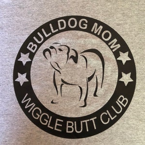 May include: Black and white graphic design on a grey t-shirt. The design features a bulldog silhouette with the text "Bulldog Mom Wiggle Butt Club" in a circle.