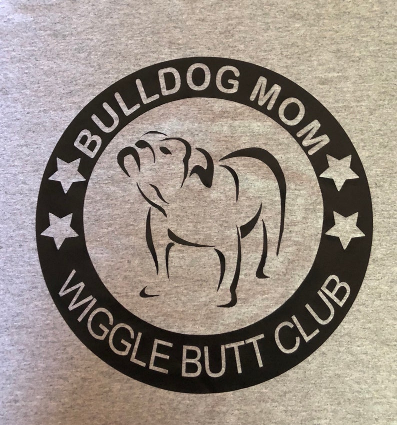 May include: Black and white graphic design on a grey t-shirt. The design features a bulldog silhouette with the text "Bulldog Mom Wiggle Butt Club" in a circle.