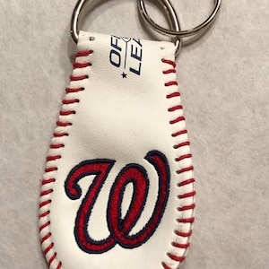 May include: White leather baseball keychain with red stitching and a blue and red embroidered "W" on the front. The keychain has a silver double ring.