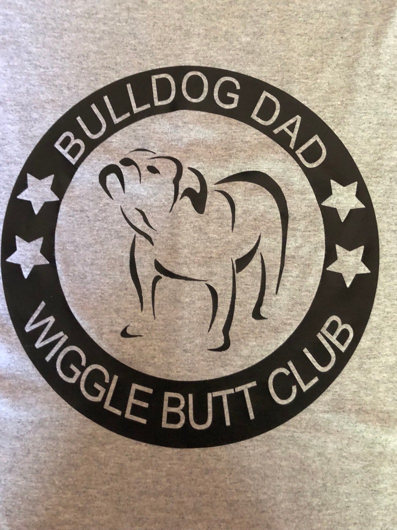 May include: Black and white graphic design of a bulldog with the text "Bulldog Dad Wiggle Butt Club" in a circle with five stars.