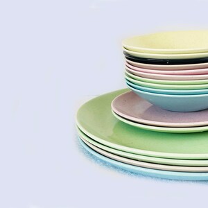 May include: A stack of pastel-colored ceramic bowls and plates. The bowls are stacked on top of the plates, and the colors range from light green to light pink. The bowls and plates are all round and have a smooth, glossy finish.
