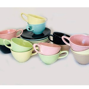 May include: A collection of vintage teacups and saucers in various pastel colors, including pink, blue, green, and yellow. The cups are stacked and arranged on a white surface.