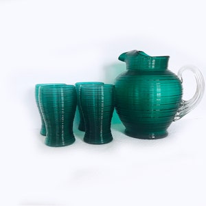 May include: A set of four teal green glasses and a matching pitcher with a clear glass handle. The glasses and pitcher have a ribbed texture.