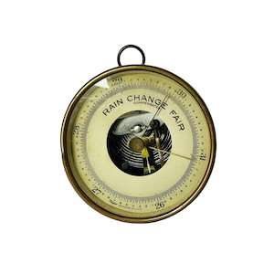 May include: A brass-colored analog barometer with a white face and black markings. The face reads "RAIN CHANGE FAIR" and has a needle pointing to "29". The barometer is made by Taylor and is manufactured in the USA.