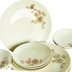 May include: A set of white ceramic dinner plates with a pine cone and branch design. The plates are in various sizes, including a large platter.