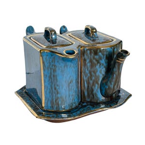 May include: A ceramic tea set with a blue and brown mottled glaze, featuring two lidded compartments and a spout. The set has gold trim and sits on a matching tray, perfect for serving tea or coffee.