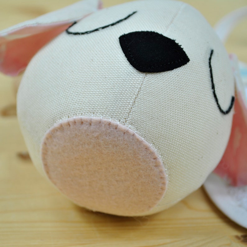 May include: A white fabric stuffed animal shaped like a dog with black embroidered eyes and a pink felt bottom.