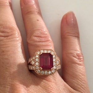 Könnte beinhalten: Ein Ring aus Roségold mit einem großen, smaragdgeschliffenen Rubin, der von einem Heiligenschein aus kleineren Diamanten umgeben ist.