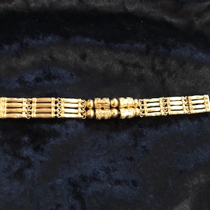 Puede incluir: Un brazalete de oro con un dise&ntilde;o de m&uacute;ltiples hebras y acentos redondos decorativos.
