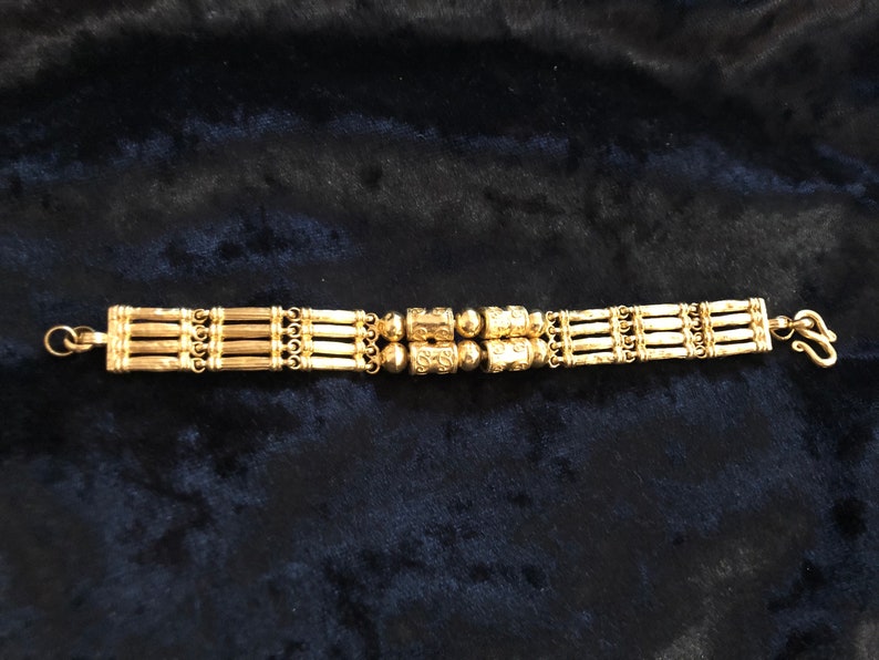 Puede incluir: Un brazalete de oro con un dise&ntilde;o de m&uacute;ltiples hebras y acentos redondos decorativos.