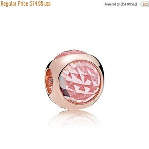 Puede incluir: Un charm de oro rosa con una cuenta de cristal rosa facetada. El charm tiene forma redonda y está diseñado para ser añadido a una pulsera o collar.