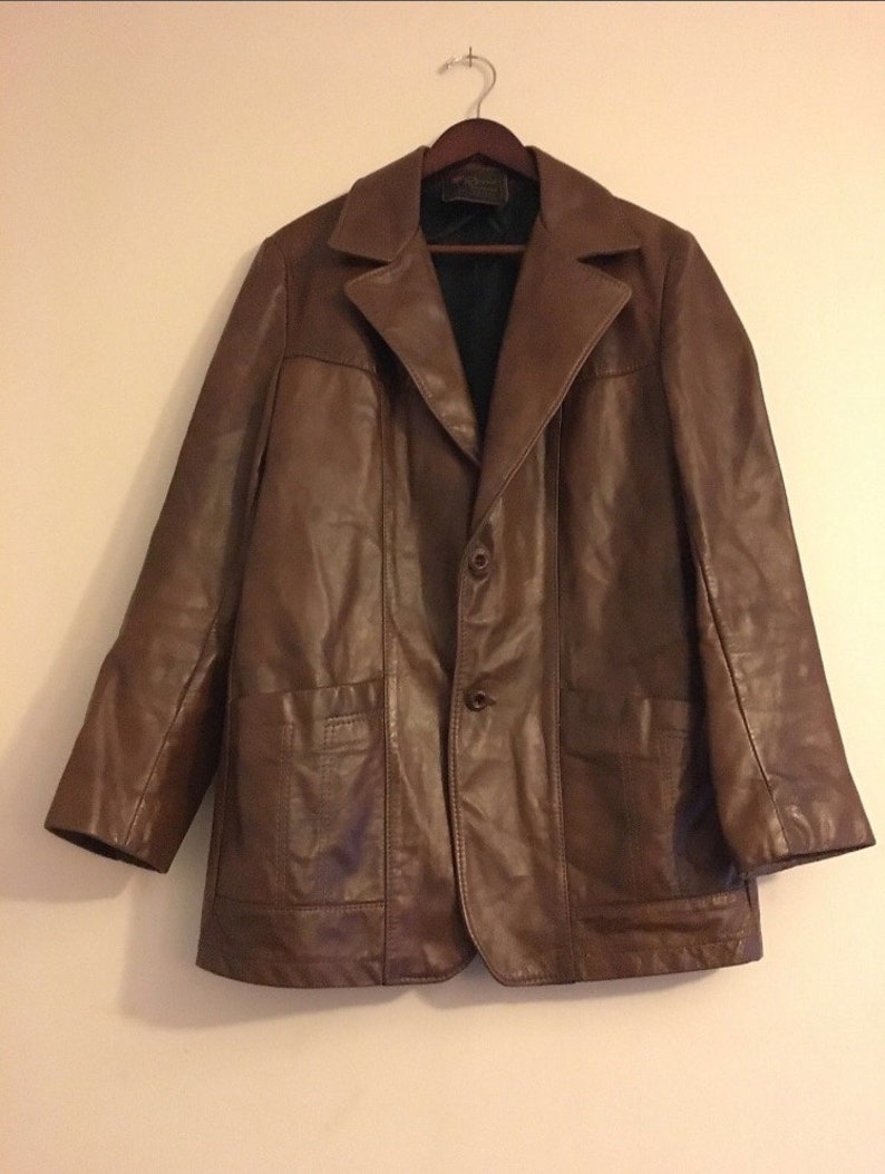 Op de afbeelding: Een bruin leren jack met knoopsluiting en twee klepzakken. Het jack heeft een klassieke stijl en is gemaakt van hoogwaardig leer.