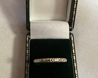 May include: A silver ring with a decorative design sits in a black ring box with a white interior.