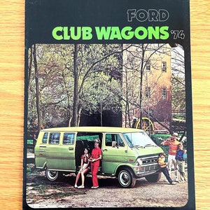 May include: A green Ford Club Wagon van from 1974 is parked in a wooded area.  Four people are standing near the van.  The van has a white Ford logo on the front.