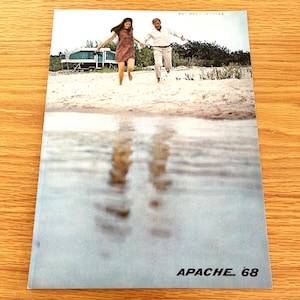 May include: A vintage magazine cover featuring a couple running on a beach with a camper van in the background. The magazine cover is titled "APACHE '68".