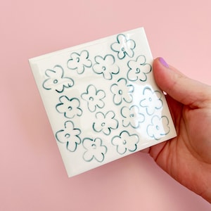 以下が含まれることがあります： 薄い青色の輪郭で描かれた花の形のパターンが施された白いステッカー用紙のシートです。