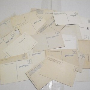 May include: A collection of vintage postcards, with the backs facing up, scattered across a surface. The postcards are primarily cream-colored with the words "POST CARD" printed on them. Some cards have a stamp box.