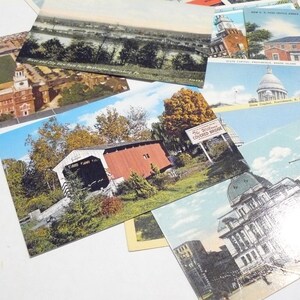 May include: A collection of vintage postcards featuring various scenic views and landmarks. The postcards showcase images of bridges, buildings, and landscapes, with a focus on architectural and natural elements. The postcards are arranged on a white surface.