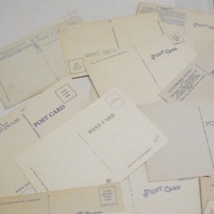 May include: A collection of vintage postcards, with the words "POST CARD" printed on the back. The postcards are cream-colored and arranged in a slightly overlapping pattern. Some have text and stamp boxes.