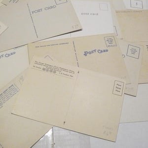May include: A collection of vintage postcards, with the words "POST CARD" printed in blue. Some cards have text about locations and places for stamps. The cards are beige and arranged on a white surface.