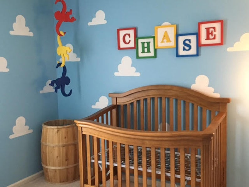 Puede incluir: Una habitaci&oacute;n de beb&eacute; con una cuna de madera, un barril de madera y un m&oacute;vil con tres monos colgando del techo. Las paredes est&aacute;n pintadas de azul y tienen nubes blancas y el nombre "CHASE" escrito en bloques de colores.