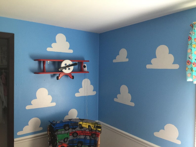 Puede incluir: Una pared azul con recortes de nubes blancas y una estanter&iacute;a de avi&oacute;n de madera roja con una h&eacute;lice blanca. La estanter&iacute;a est&aacute; montada en la pared.