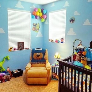 Puede incluir: Una habitaci&oacute;n de beb&eacute; decorada con un tema de nubes azules y blancas. La habitaci&oacute;n cuenta con una cuna con un juego de cama de Monsters Inc., un juguete de dinosaurio de peluche, una mecedora con una manta de Woody de Toy Story y una l&aacute;mpara con una pantalla que presenta un personaje de dibujos animados.