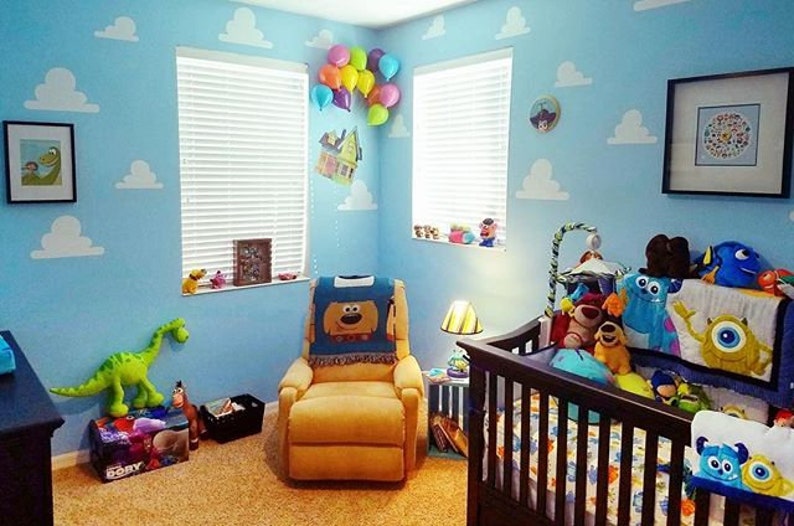 Puede incluir: Una habitaci&oacute;n de beb&eacute; decorada con un tema de nubes azules y blancas. La habitaci&oacute;n cuenta con una cuna con un juego de cama de Monsters Inc., un juguete de dinosaurio de peluche, una mecedora con una manta de Woody de Toy Story y una l&aacute;mpara con una pantalla que presenta un personaje de dibujos animados.