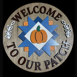 May include: Welcome to Our Patch sign with a blue and orange patchwork design and a pumpkin in the center. The sign is made of wood and has a rustic look.