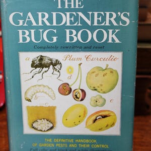 May include: A vintage book titled "The Gardener's Bug Book" with a teal cover. The cover features illustrations of insects and fruits, including a plum curculio. The book is a definitive handbook on garden pests and their control, written by Cynthia Westcott.