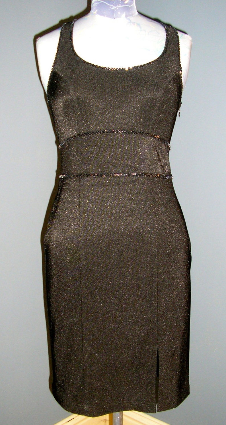 May include: A black sleeveless dress with a sparkly trim around the neckline and waist. The dress has a slit up the front.
