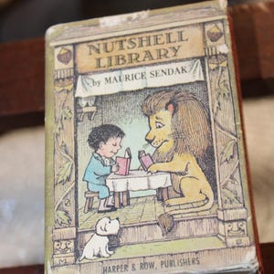 May include: A vintage children's book titled "Nutshell Library" by Maurice Sendak. The cover features a colorful illustration of a boy and a lion reading at a table, with a small dog. Published by Harper & Row.