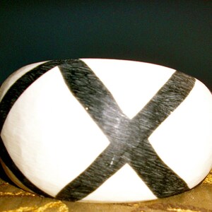 May include: A white bangle bracelet with a black X design. The bangle is made of a smooth, rounded material.