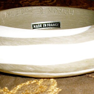 May include: A wide, brown and white striped bangle bracelet with the text "Made in France" on a label.