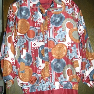May include: A red and white patterned jacket with a zipper closure. The pattern features a variety of shapes and colors, including circles, squares, and flowers. The jacket is made of a silky material.