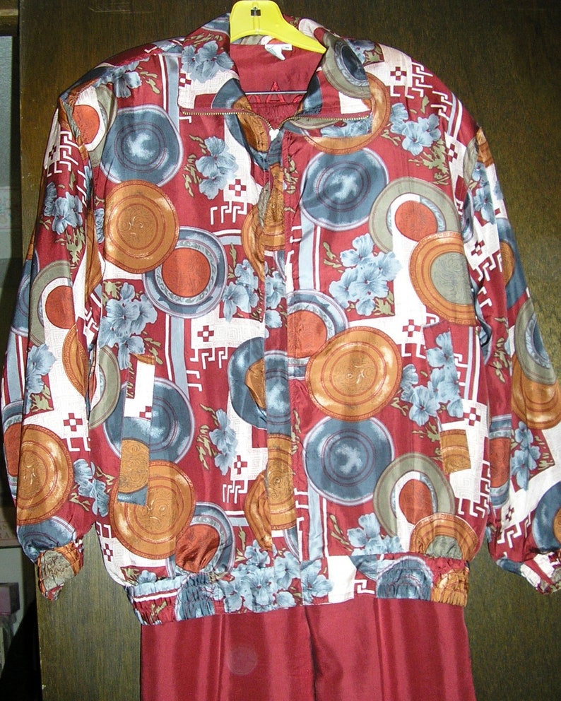 May include: A red and white patterned jacket with a zipper closure. The pattern features a variety of shapes and colors, including circles, squares, and flowers. The jacket is made of a silky material.