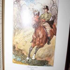 K&ouml;nnte beinhalten: Eine Buchillustration zeigt einen Mann in gr&uuml;ner Jacke und Zylinder auf einem braunen Pferd. Das Pferd springt &uuml;ber einen Bach. Das Kunstwerk ist im Vintage-Stil gehalten, mit ged&auml;mpften Farben und einer detaillierten Landschaft.