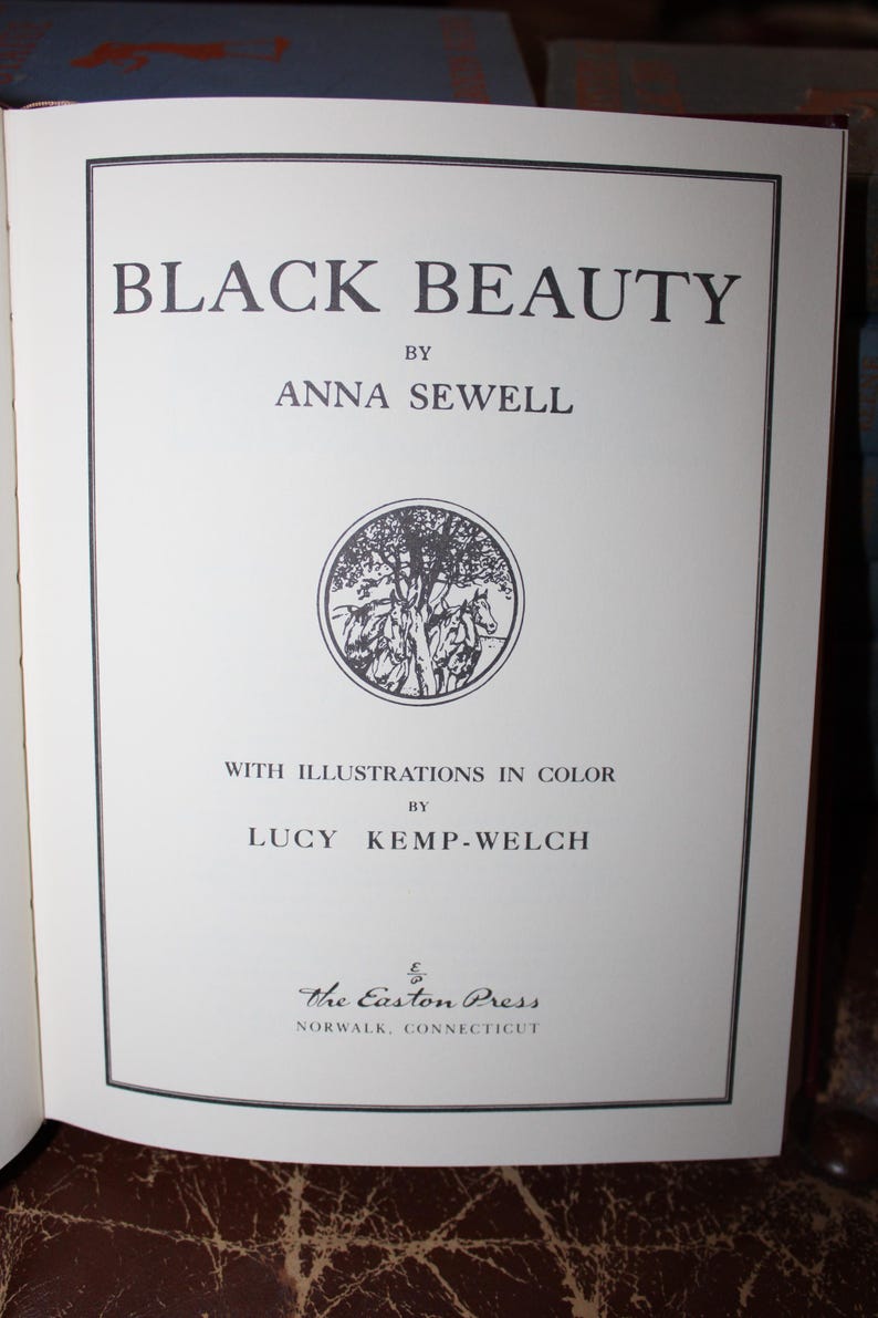 K&ouml;nnte beinhalten: Titelseite des Buches "Black Beauty" von Anna Sewell, mit Illustrationen von Lucy Kemp-Welch. Der Titel ist gro&szlig; geschrieben. Eine runde Illustration von Pferden und B&auml;umen ist enthalten. Ver&ouml;ffentlicht von The Easton Press, Norwalk, Connecticut.