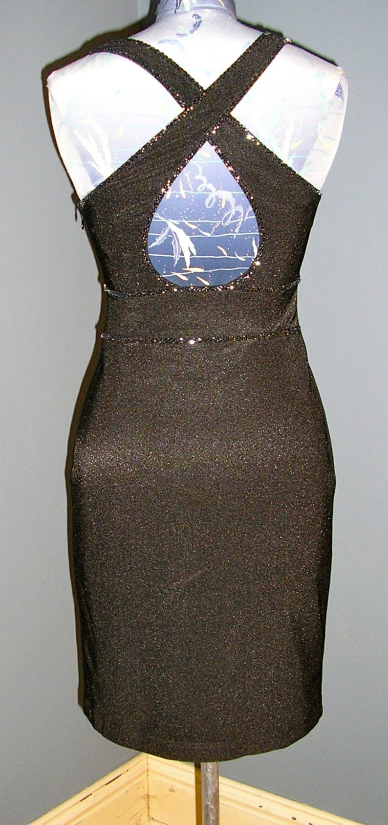 May include: A black sparkly dress with a criss-cross back and a keyhole cutout in the back. The dress has a fitted silhouette and a short length.