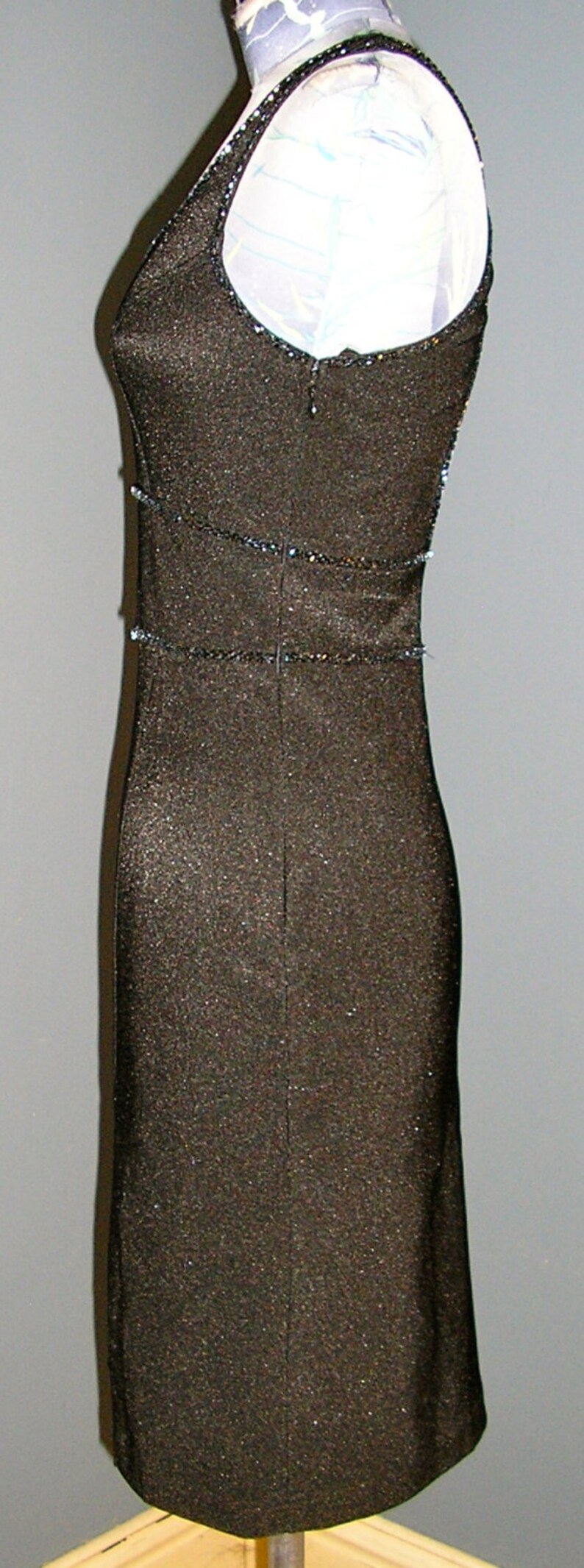 May include: A black sequined sleeveless dress with a scoop neck and a fitted silhouette. The dress has a beaded trim around the neckline and waist.