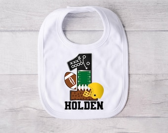 May include: White bib with a black and green football jersey design, a brown football, and a yellow helmet. The number one is on the jersey with the name Holden below.