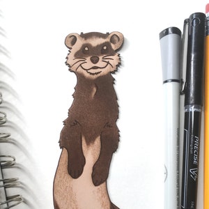 May include: A brown and tan leather bookmark shaped like a ferret standing on its hind legs. The ferret has a long tail and a friendly expression.