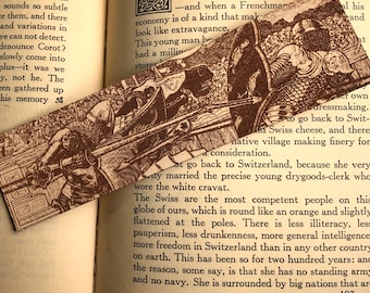 May include: A brown bookmark with a detailed illustration of a medieval battle scene. The bookmark features a knight in armor on horseback, charging into battle with a sword raised. The background includes other knights, soldiers, and horses.