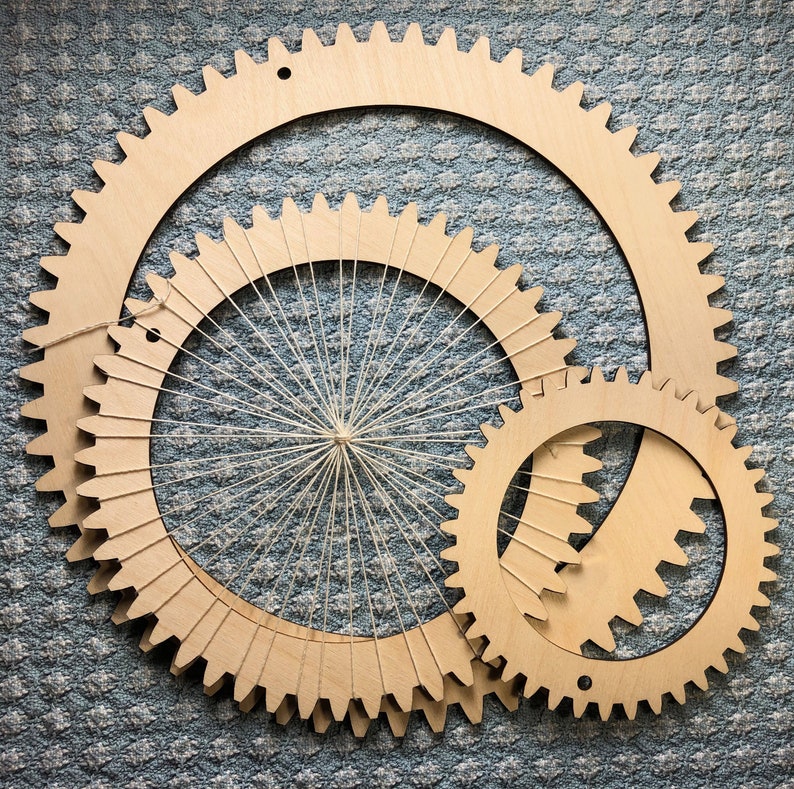 The photograph shows 3 wood circle looms of different sizes resting on a blue and white fabric. The middle sized circle loom is already warped as an example of how it looks warped. Each circle loom has a small hanging hole.