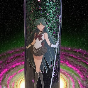 May include: A tall, cylindrical tumbler with a glittery green and black design. The tumbler features a full-body illustration of a character with long green hair, a white and brown outfit, and a staff. The background is a galaxy.