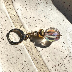 May include: Gold hoop earring with a clear iridescent glass bead and gold accents.