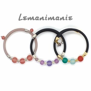 May include: Three bracelets with different colored beads. The bracelets are made of black and gray elastic and have gold accents. The beads are pink, purple, and blue.